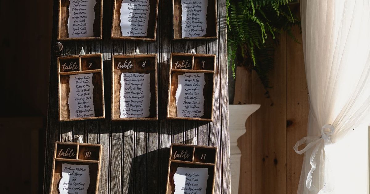 Rustic wooden wedding seating chart displayed beside a potted plant in the sunlight