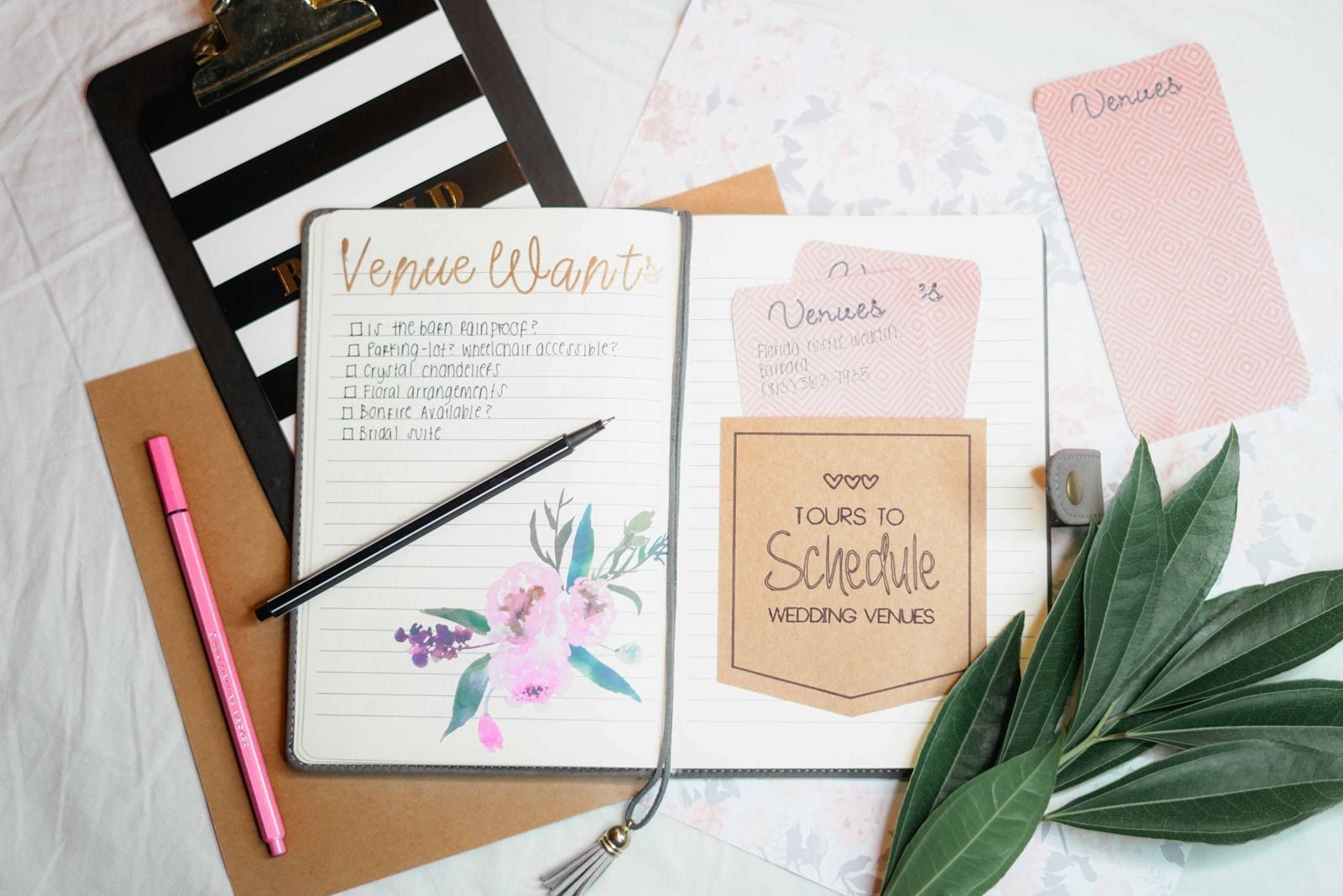 Flat lay of a wedding planning journal, dried leaves and stationery on a table