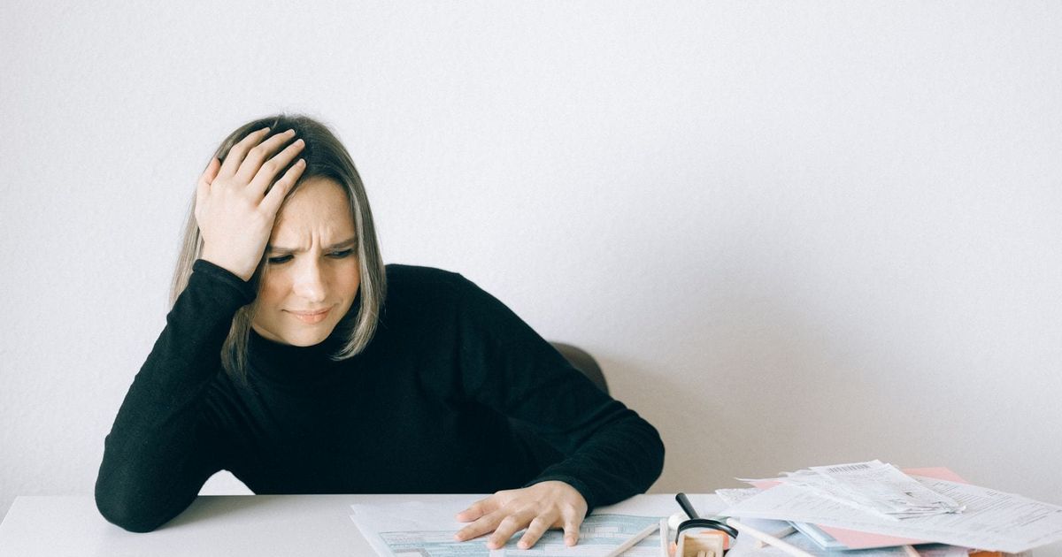 Woman sitting at a table with her hand on her head, overwhelmed by paperwork