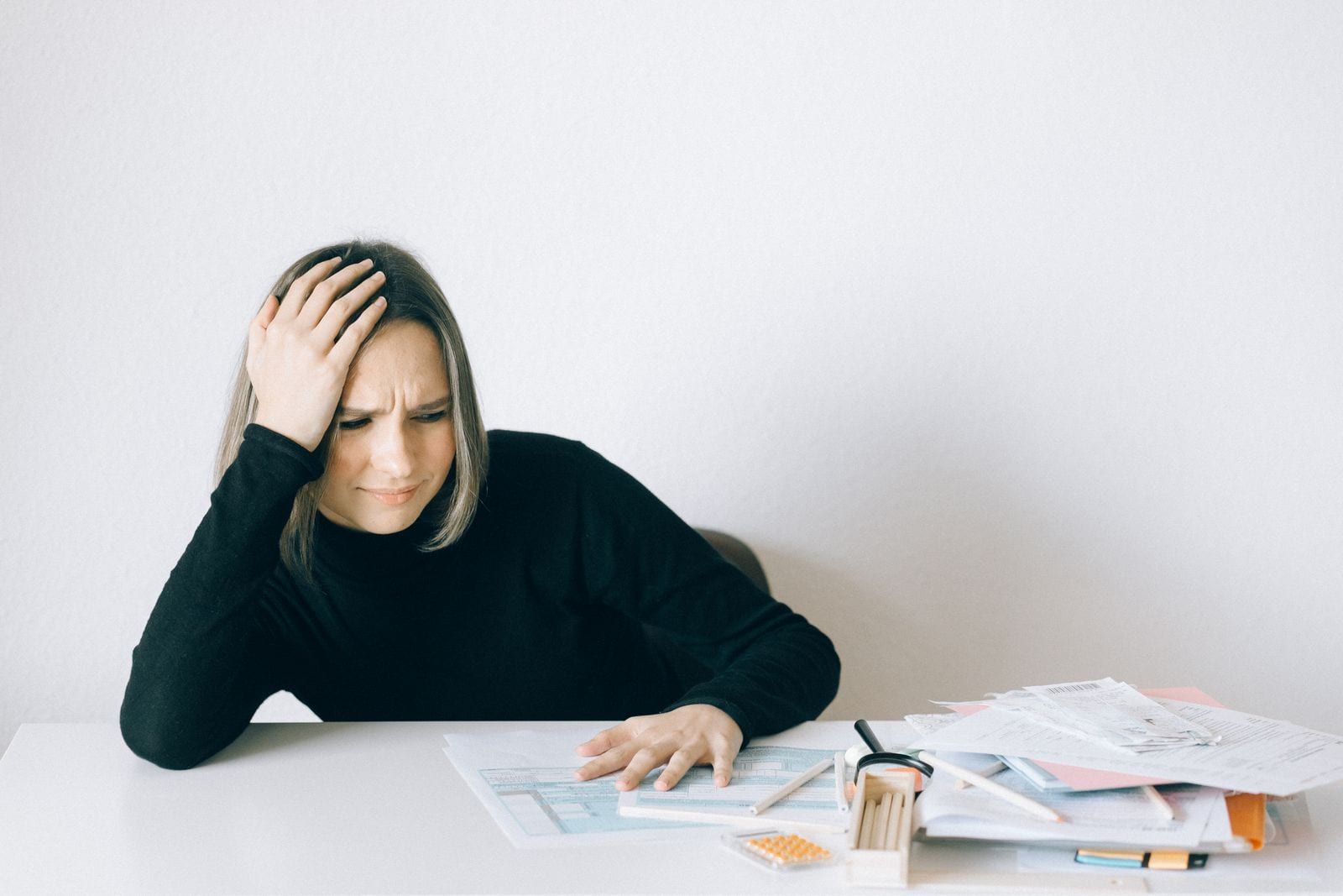 Woman sitting at a table with her hand on her head, overwhelmed by paperwork