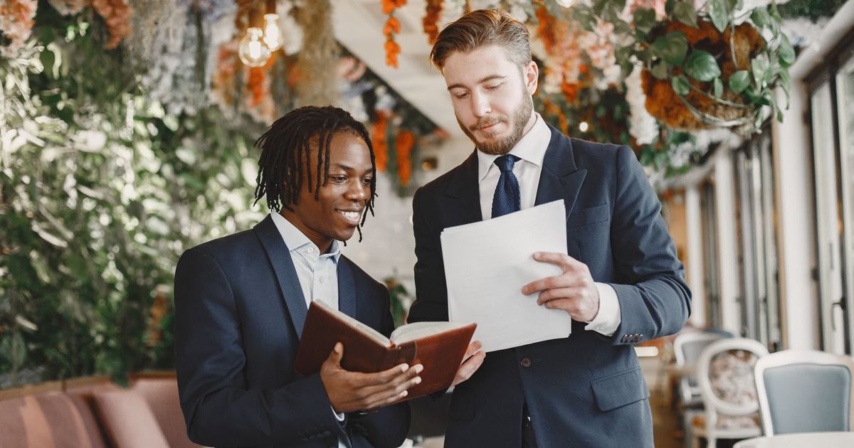 Two suppliers in suits reviewing paperwork together at a decorated reception venue